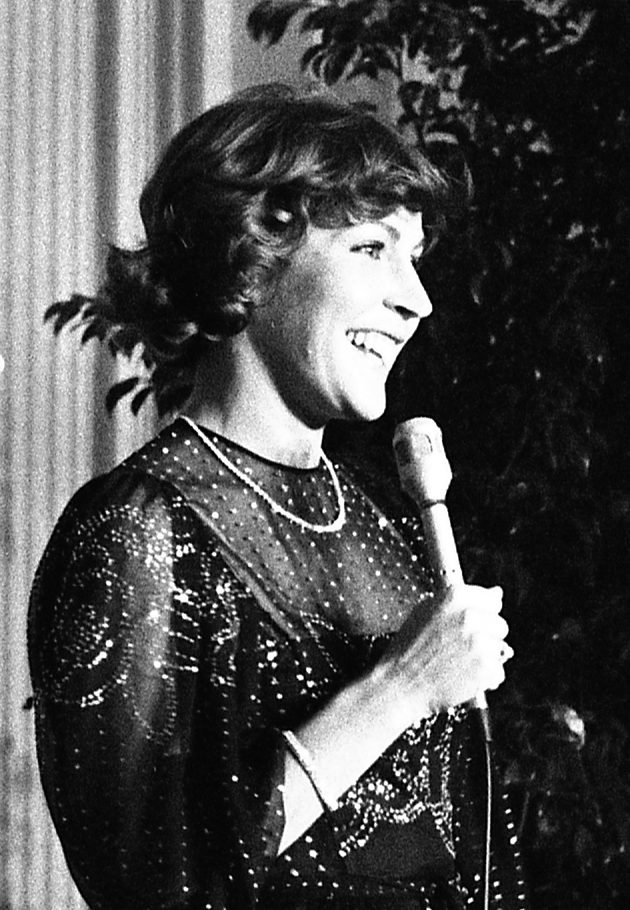 Helen Reddy smiling and holding a microphone while singing on stage at the White House in January 1976, the voice behind Delta Dawn and Angie Baby