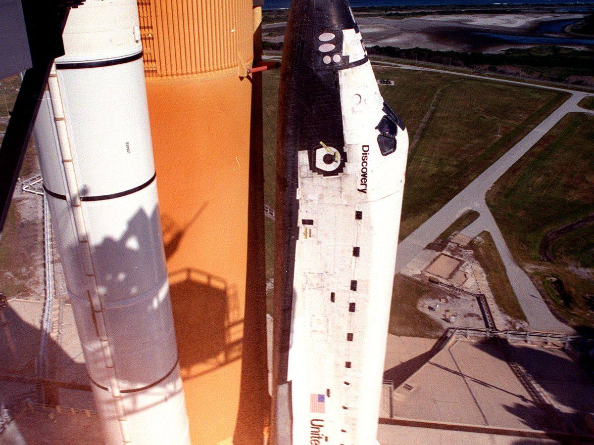 A Space Shuttle Discovery launch with the orbiter rising beside its orange tank and white booster, the vehicle at whose launch site Elton John played Rocket Man in 1998