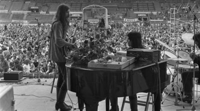 A massive crowd watches a live band perform at an Amsterdam stadium concert in 1972, the era this 70s music quiz puts to the test