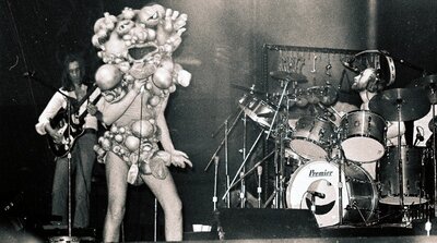 Genesis performing The Lamb Lies Down on Broadway in Chicago, November 1974, Peter Gabriel in full costume with Phil Collins on drums, the kind of theatrical concept-album staging that defined 70s progressive rock